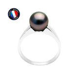 La Perlinea Bague IRINA, en or blanc avec une perle noire de Tahiti de 8/9 mm, est présentée sur un fond blanc. Le logo circulaire de l'Artisan Bijoutier Français apparaît dans le coin supérieur gauche.