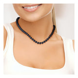 Une femme vêtue d'un haut blanc sans manches sourit doucement, portant le Collier NOELYSE de Perline - un collier argenté avec des perles noires de 8/9 mm et un fermoir en forme de homard. L'image se concentre sur son cou, ses épaules et une partie de son visage.