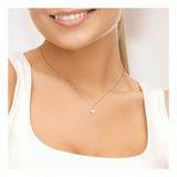 Une femme portant un haut blanc et le Perlinea Pendentif ORÉA - un collier artisanal français en or blanc avec une perle de culture de 6-7 mm - sourit doucement, le bas de son visage étant visible.