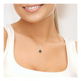 Une femme vêtue d'un haut blanc sans manches sourit, mettant en valeur le Perlinea Collier Perles de Culture de Tahiti 8-9 mm - un délicat collier en argent avec une petite étoile, un pendentif en forme de larme vert foncé et des perles de culture de Tahiti. L'accent est mis sur son cou.
