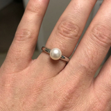 Bague jonc en argent 925 ornée d'une perle de culture blanche, portée à l'annulaire.