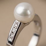 Bague or blanc 9 carats, gros plan sur sertissage trois diamants et perle de culture blanche.