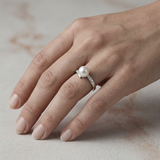 Bague en or blanc avec perle de culture blanche et diamants portée à l'annulaire.