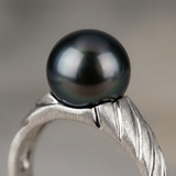Gros plan sur la perle de Tahiti noire d'une bague en or blanc 9 carats au bandeau texturé.