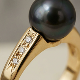 Gros plan sur le sertissage de trois diamants en or jaune et la perle noire de Tahiti.