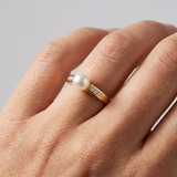 Bague or jaune 9 carats avec perle de culture blanche et diamants portée à la main.