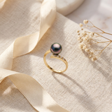 Bague or jaune 9 carats avec perle de Tahiti noire irisée et diamants, posée sur tissu.