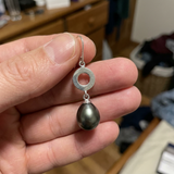 Boucle d'oreille pendante argent 925 avec anneau et perle noire baroque, tenue en main.