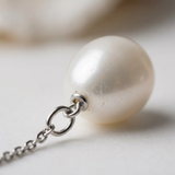 Gros plan sur la perle de culture blanche d'une boucle d'oreille pendante en or blanc.