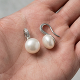 Boucles d'oreilles argent 925 avec perles blanches rondes et crochets pavés, posées dans une paume.