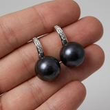 Boucles d'oreilles en argent 925 avec perles noires tenues dans une main.