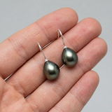 Boucles d'oreilles crochets argent 925 avec perles de Tahiti grises ovales, tenues dans une main.