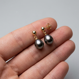 Boucles d'oreilles or jaune 9 carats avec perles de Tahiti grises baroques, tenues dans une main.