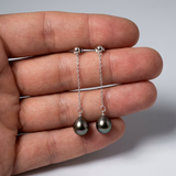 Boucles d'oreilles pendantes argent 925 et perles de Tahiti baroques présentées dans une main.