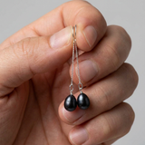 Boucles d'oreilles pendantes or blanc 9 carats avec perles de culture noires de Tahiti, tenues en main.
