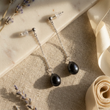 Boucles d'oreilles pendantes or blanc 9 carats et perles noires sur chaîne fine.