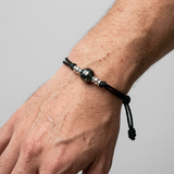 Bracelet homme en coton ciré noir avec perle de Tahiti et nœuds argent, porté au poignet.