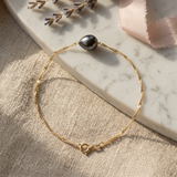 Bracelet en or jaune 9 carats avec une perle de Tahiti grise, posé sur marbre.