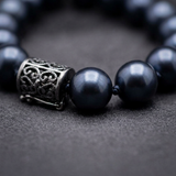 Gros plan sur bracelet perles noires et charm cylindrique en argent 925 gravé.