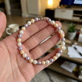 Bracelet perles d'eau douce multicolores blanc rose lavande avec fermoir argent 925, tenu dans une main.