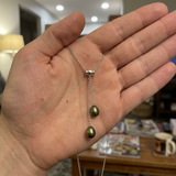Collier toi et moi en argent 925 tenu dans une paume, deux perles de culture vert intense en goutte.