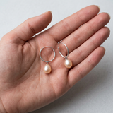 Boucles d'oreilles créoles argent 925 avec perles de culture roses, présentées dans une main.