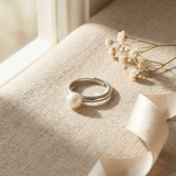 Bague jonc argent 925 à perle de culture blanche posée sur tissu beige.