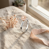 Bague jonc argent 925 surmontée d'une perle de culture rose, posée sur lin beige.