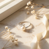 Bague or blanc 9 carats avec perle de culture blanche et diamants, posée sur marbre.