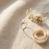 Bague or blanc 9 carats et perle de culture rose, posée sur lin beige avec fleurs séchées.