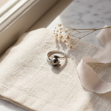 Bague en or blanc 9 carats avec perle de Tahiti grise, posée sur tissu lin.
