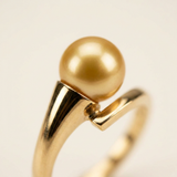 Gros plan sur le sertissage tension d'une bague en or jaune 9 carats et perle dorée.