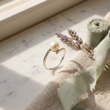 Bague or blanc 9 carats à perle de culture blanche, anneau fin ouvert posé sur marbre.
