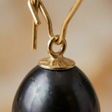 Gros plan sur la perle poire noire de Tahiti et son anneau de suspension en or jaune.
