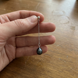 Boucle d'oreille pendante en or blanc avec chaîne fine et perle noire de culture.