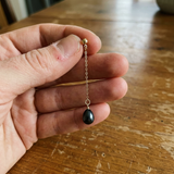 Boucle d'oreille pendante or jaune 9 carats chaîne fine et perle noire de Tahiti, tenue en main.