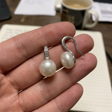 Boucles d'oreilles argent 925 à perles blanches rondes, tenues dans une main.