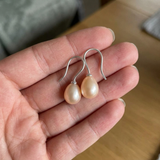Boucles d'oreilles argent 925 avec perles de culture roses en forme de goutte, tenues dans une main.