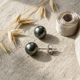 Boucles d'oreilles bouton en argent 925 avec perles de Tahiti grises, présentées sur tissu naturel.