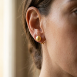 Boucles d'oreilles bouton en or jaune et perle de culture dorée portées à l'oreille.