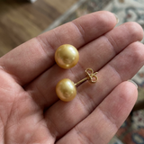 Boucles d'oreilles bouton en or jaune 9 carats avec perles de culture dorées, tenues dans une main.