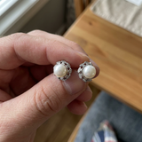 Boucles d'oreilles argent 925 avec perles blanches rondes serties de feuilles pavées, tenues en main.