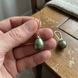 Boucles d'oreilles or jaune 9 carats avec perles de culture poire vertes, tenues en main.