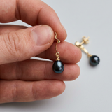 Boucles d'oreilles or jaune et perles de culture noires de Tahiti tenues en main.