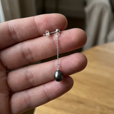 Boucles d'oreilles pendantes argent 925 et perle de Tahiti noire, tenues dans une main.