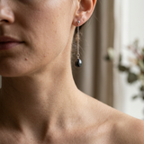 Boucles d'oreilles pendantes en or blanc 9 carats avec perle noire de Tahiti portées à l'oreille.