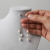 Boucles d'oreilles pendantes or blanc 9 carats à chaînes et perles de culture blanches, tenues à la main.