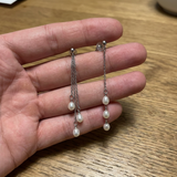 Boucles d'oreilles pendantes en or blanc 9 carats avec perles de culture blanches, tenues dans une main.