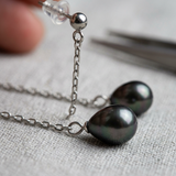 Boucles d'oreilles pendantes or blanc 9 carats avec perles noires de Tahiti sur chaîne fine.