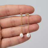 Boucles d'oreilles pendantes or jaune 9 carats, chaîne fine et perle blanche en goutte, tenues dans une main.
